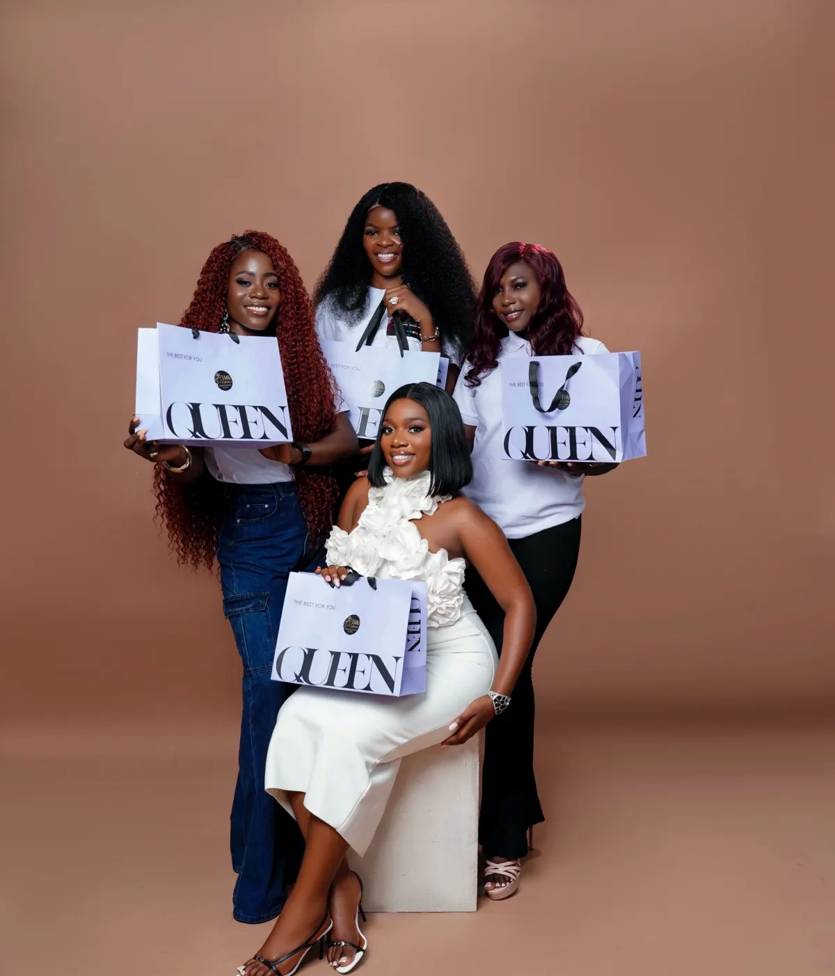 Four women in VMK hair — copper curls, kinky curly, burgundy waves and a sleek bob — smiling with lilac QUEEN bags